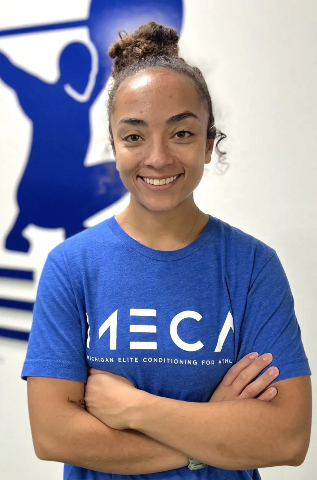 a woman with her arms crossed in front of a blue gym sign.