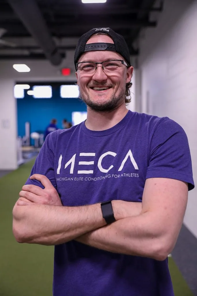 a MECA employee in a purple shirt and glasses smiles at the camera.
