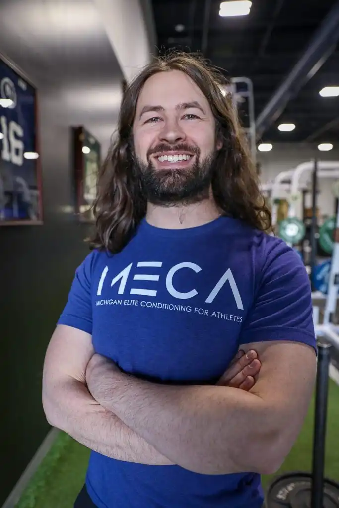 a man with long hair and a beard stands in a gym.