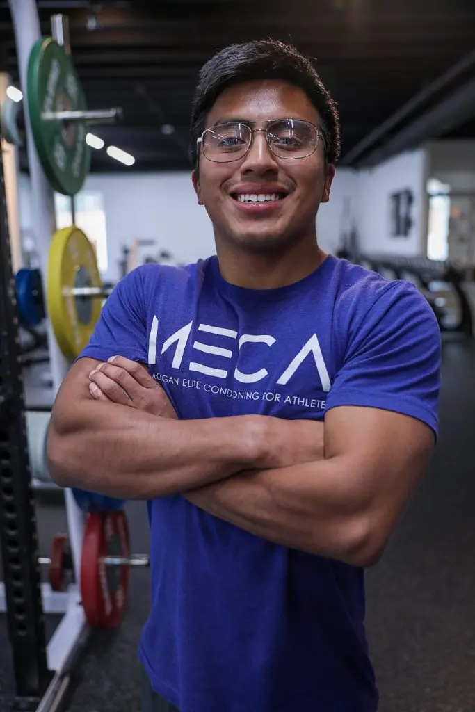 a man in a blue shirt and glasses stands in a gym.