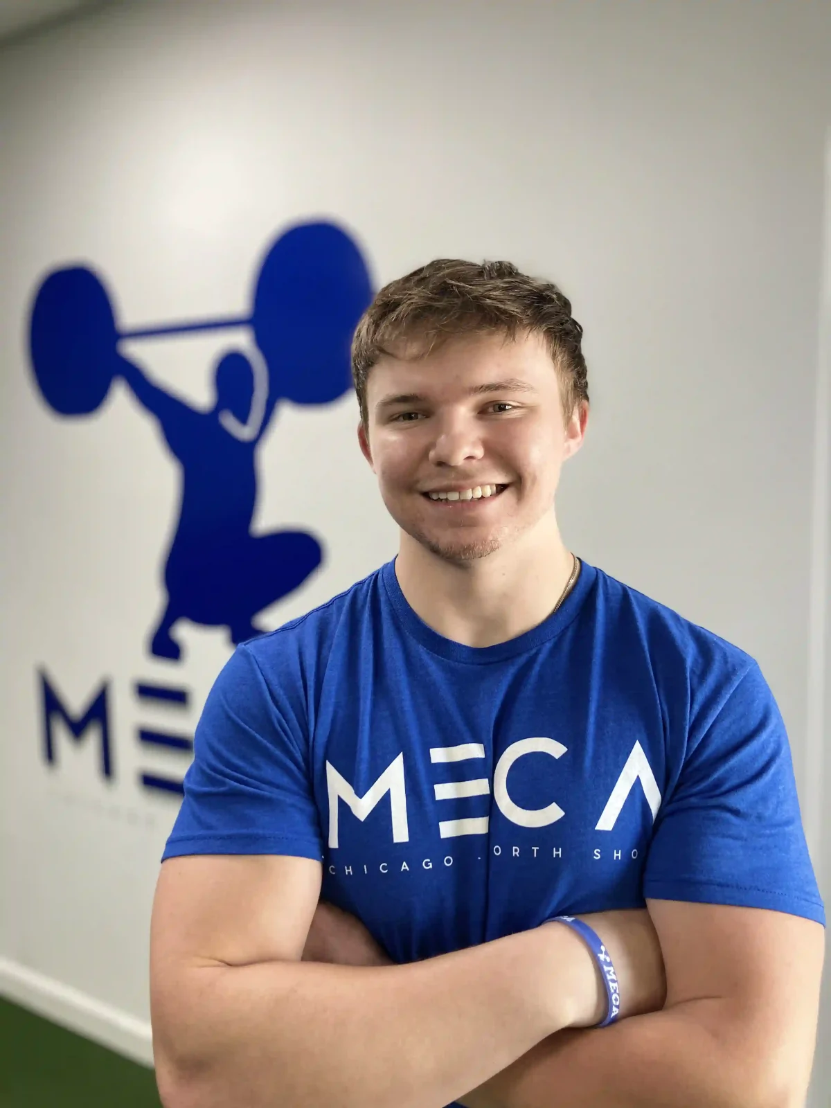 a man in a blue shirt stands in front of a wall with a barbell behind him.