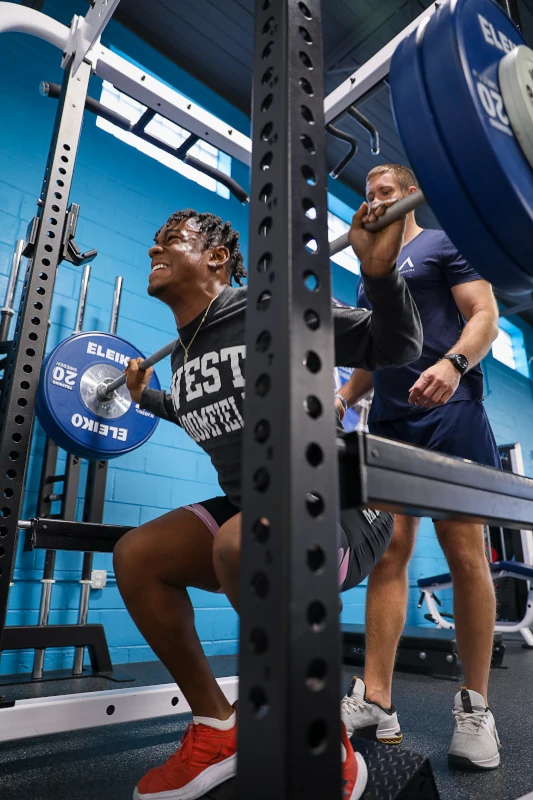 A MECA fitness coach trains an athlete and assists him with squats.