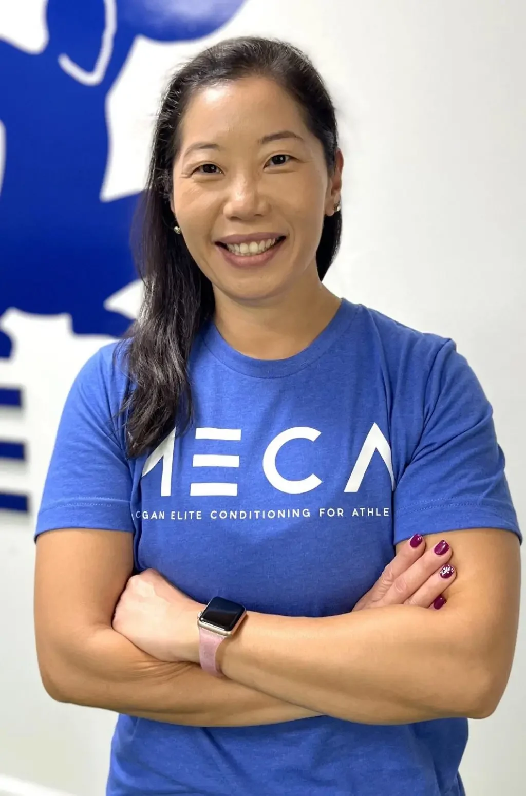 a woman with her arms crossed standing in front of a blue wall. She is an admin officer at MECA gym